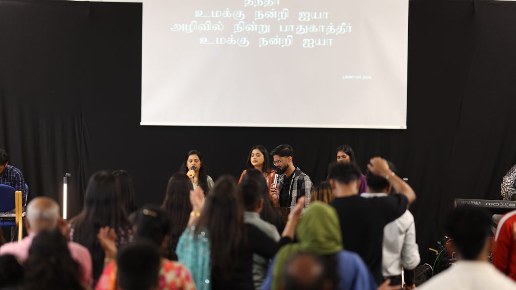 Congregation worshipping in front of the stage while Tamil song lyrics are projected on the screen