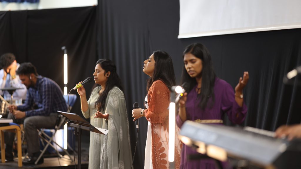 Three worship singers with eyes closed, singing between glowing light tubes