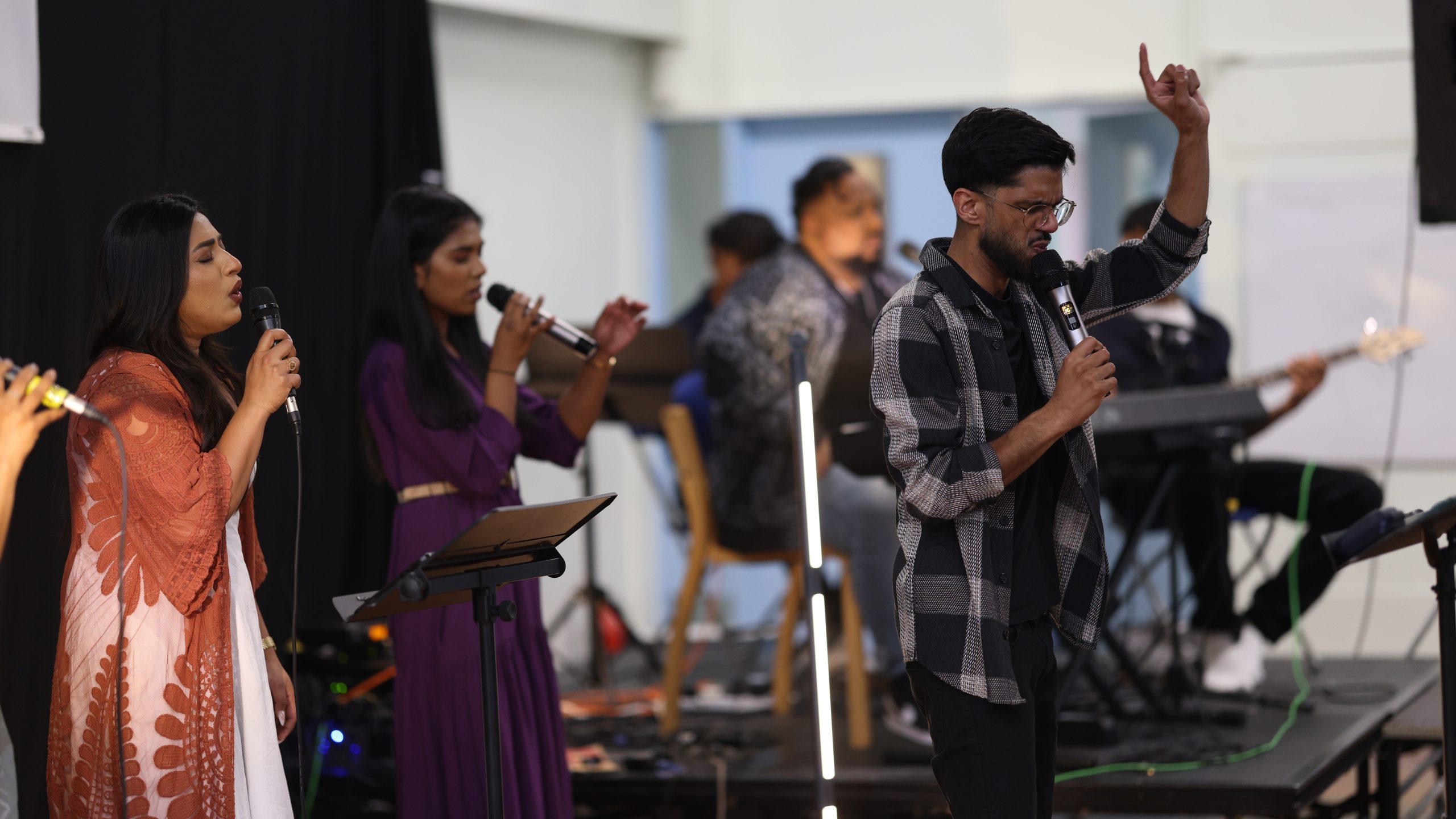 Worship team singing on stage, one singer pointing upward
