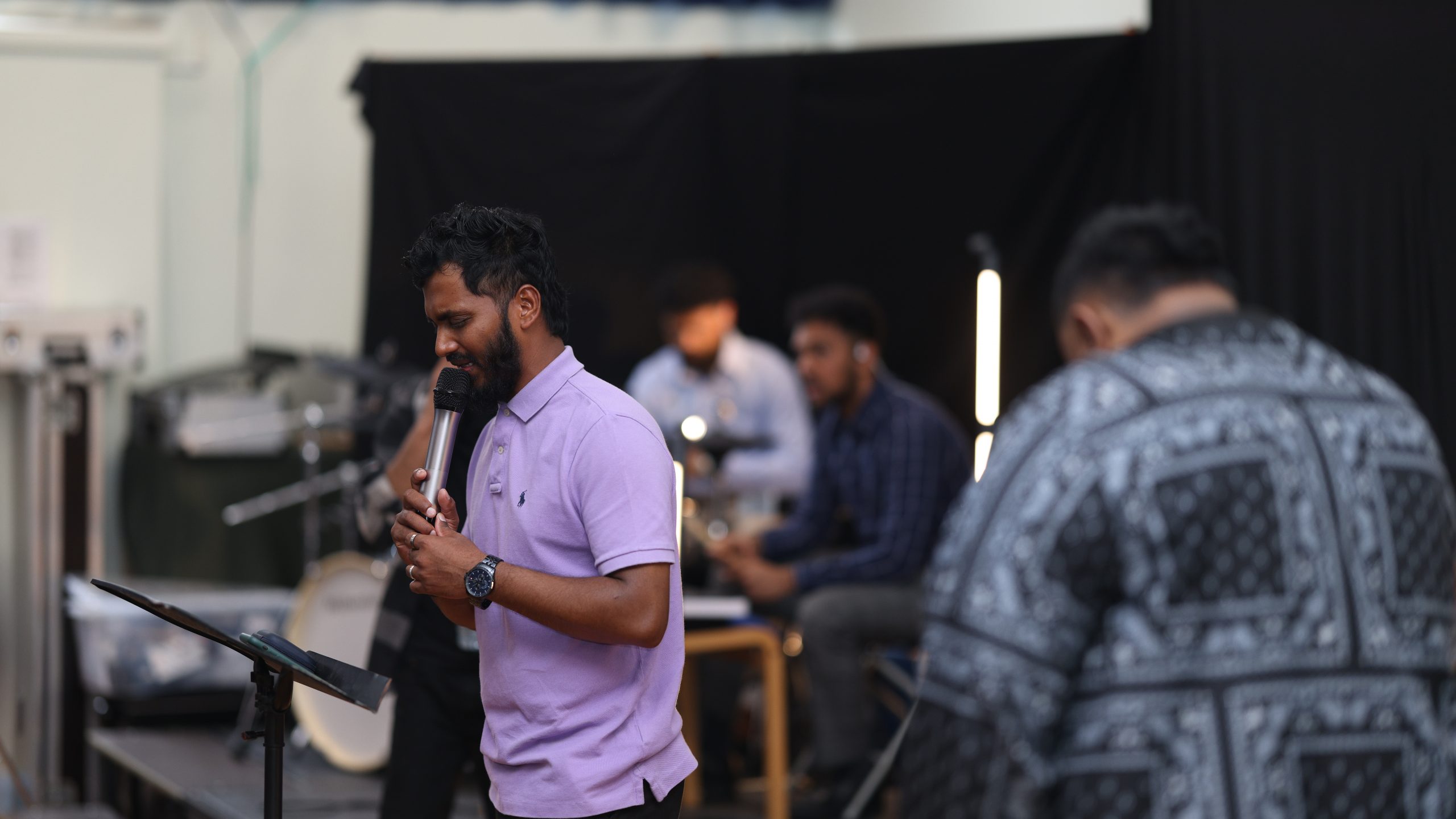 Worship leader in a lilac shirt singing with the band